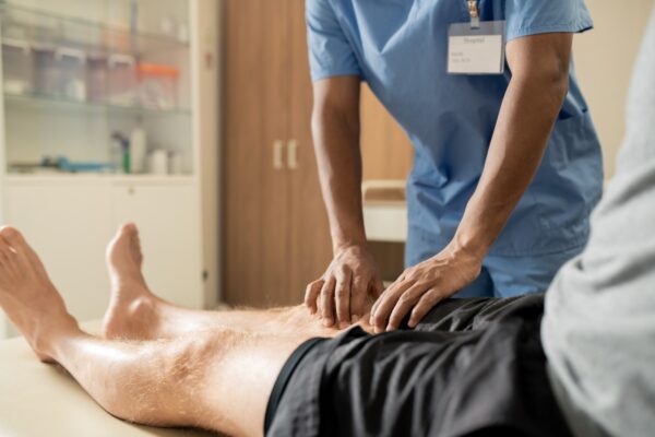 患者の膝をチェックする青いユニフォームの臨床医