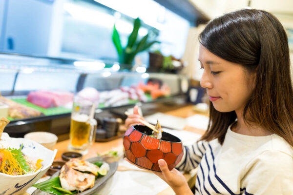 アジア人女性が日本食丼ぶりを食べている写真