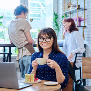 女性がカフェでコーヒーを楽しみながらカメラに笑顔を向けている写真