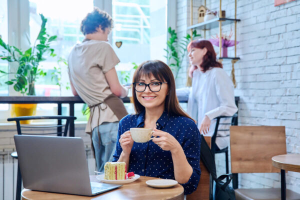 女性がカフェでコーヒーを楽しみながらカメラに笑顔を向けている写真